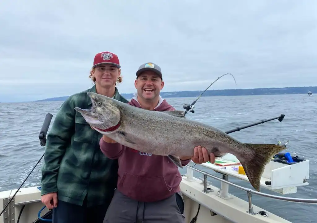 Two anglers holding a large salmon during a Seattle salmon fishing charter on Puget Sound.
